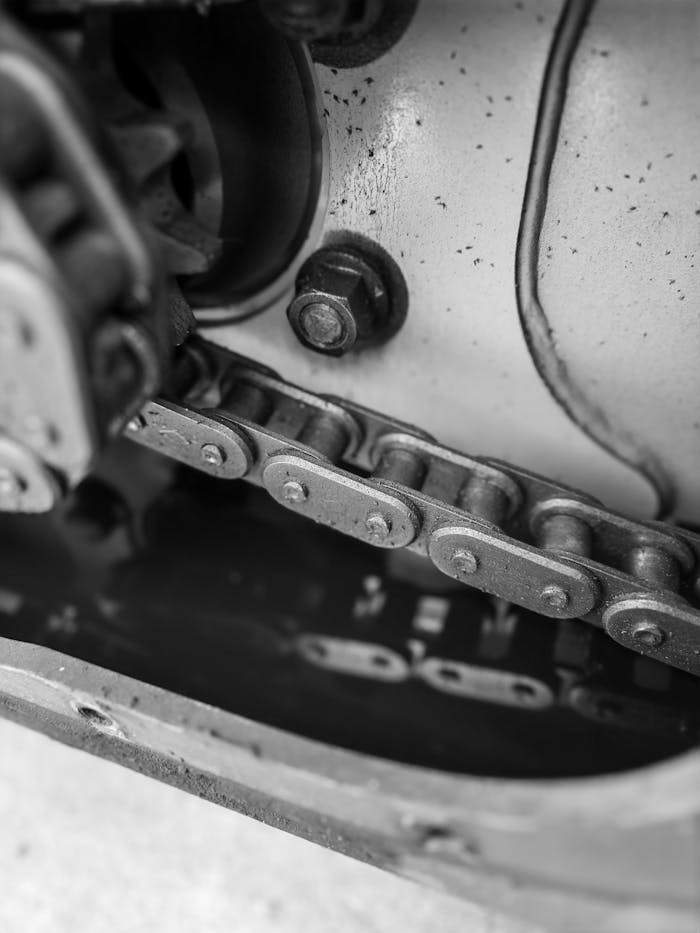Detailed black and white photo of a chain gear in an industrial machine, reflecting in oil.